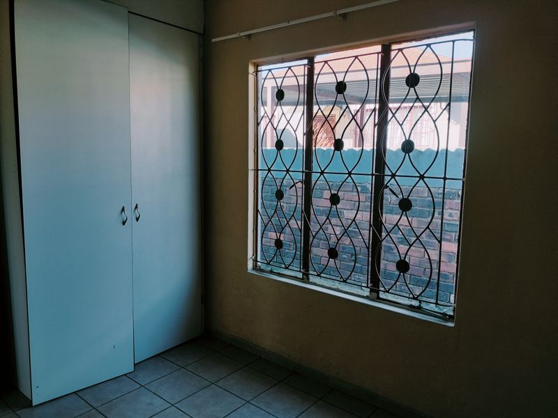 An empty bedroom featuring tiled flooring, a built-in wardrobe, and a window fitted with decorative security burglar bars.
