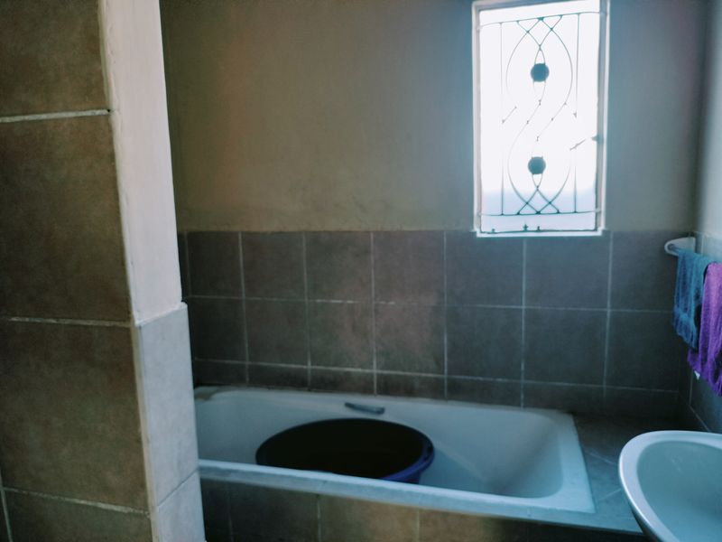 A functional bathroom featuring a built-in bathtub, a washbasin, and tiled wall finishes with a security-grille window.