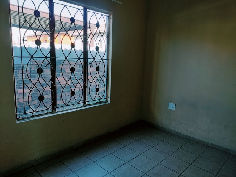 An empty bedroom featuring tiled flooring, a window with decorative security burglar bars, and neutral wall finishes.