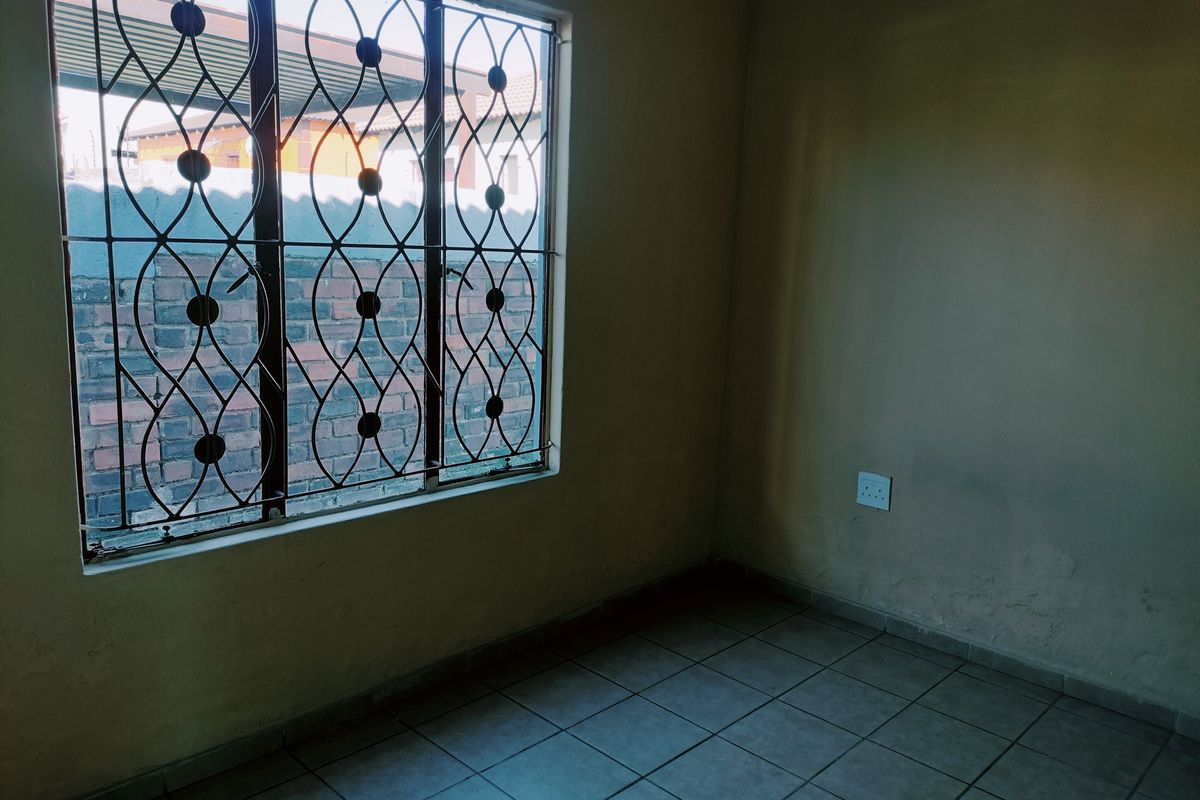 An empty bedroom featuring tiled flooring, a window with decorative security burglar bars, and neutral wall finishes.