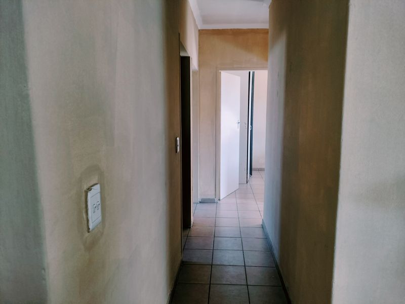 A narrow hallway featuring tiled flooring and unfinished wall surfaces, leading to an adjacent room with an open door.