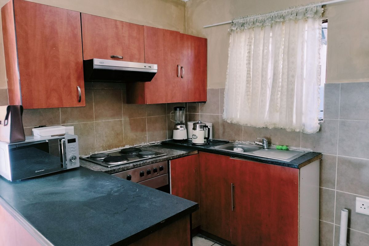 A compact kitchen featuring laminate cabinetry, built-in oven with hob, extractor fan, and tiled backsplash, requiring cosmetic updates to improve overall finish.