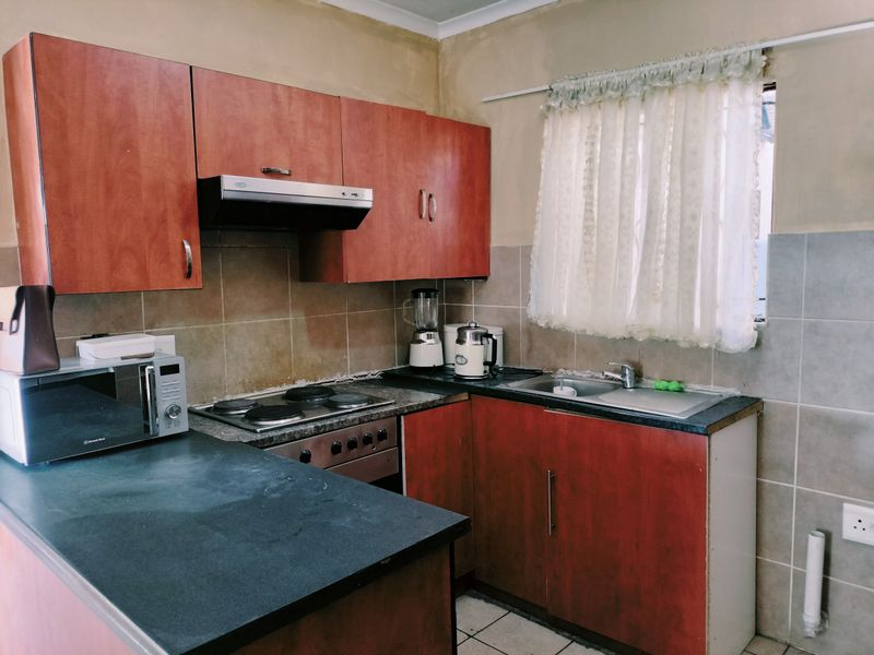A compact kitchen featuring laminate cabinetry, built-in oven with hob, extractor fan, and tiled backsplash, requiring cosmetic updates to improve overall finish.