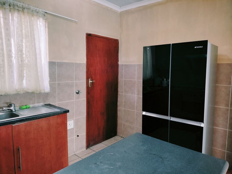 A functional kitchen area featuring tiled splashbacks, built-in cabinetry, and a stainless steel sink, requiring cosmetic updates to modernize the space.