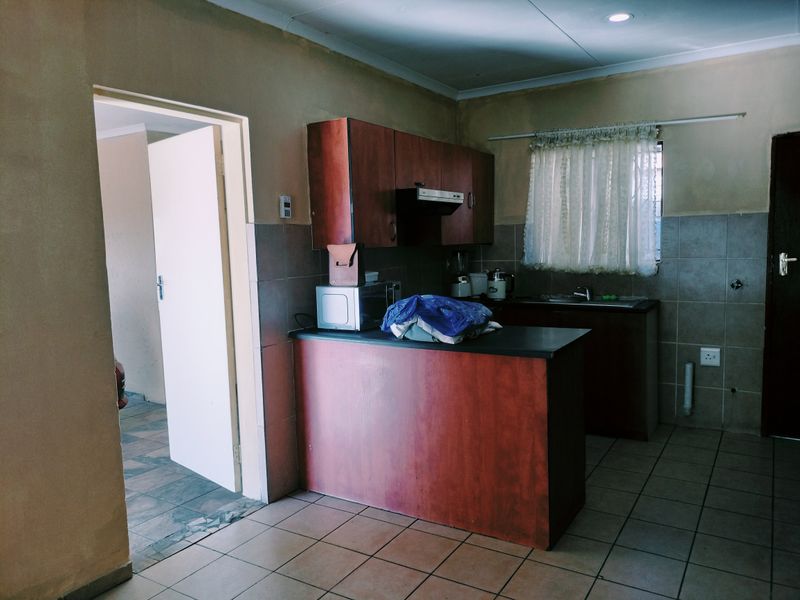 A functional kitchen featuring built-in wooden cabinetry, tiled splashbacks, and a breakfast counter, offering a practical layout with potential for modern cosmetic updates.