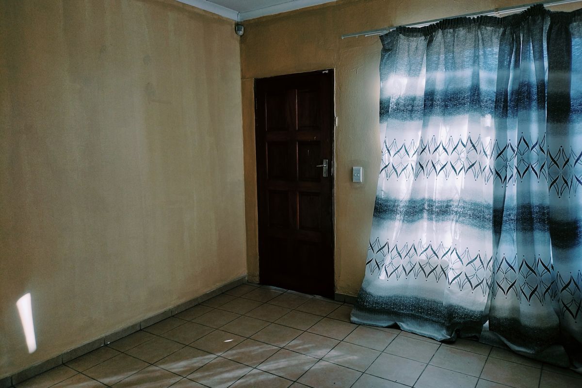 An empty living room featuring tiled flooring and a timber door, requiring cosmetic updates to the wall finishes.