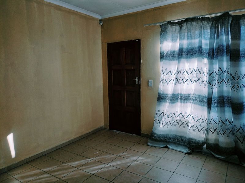 An empty living room featuring tiled flooring and a timber door, requiring cosmetic updates to the wall finishes.