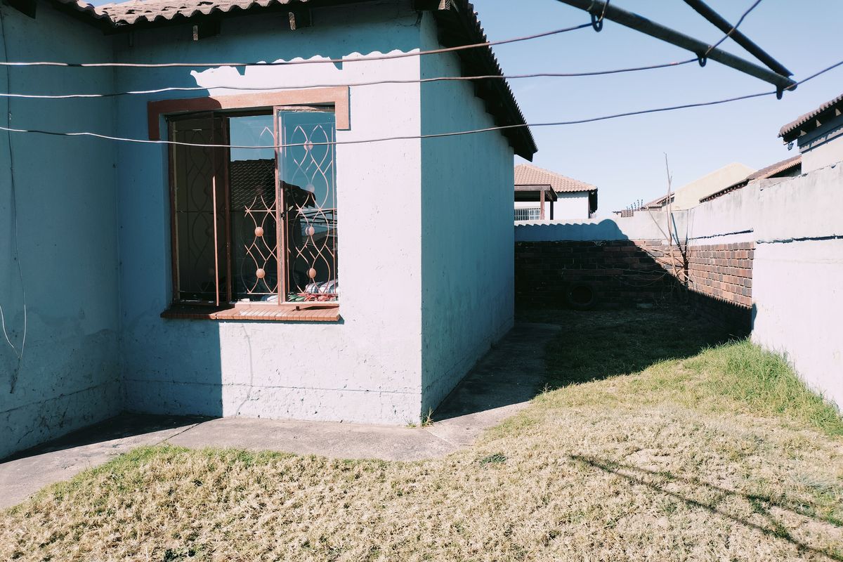 Rear view of the property showing a small garden area, concrete pathway, and brick boundary wall with visible exterior wall maintenance required.