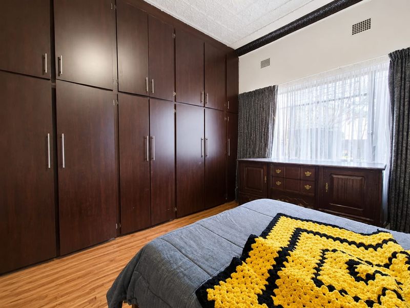 A well-maintained bedroom featuring extensive floor-to-ceiling built-in cabinetry, laminate flooring, and a decorative pressed metal ceiling with ornate cornice detailing.