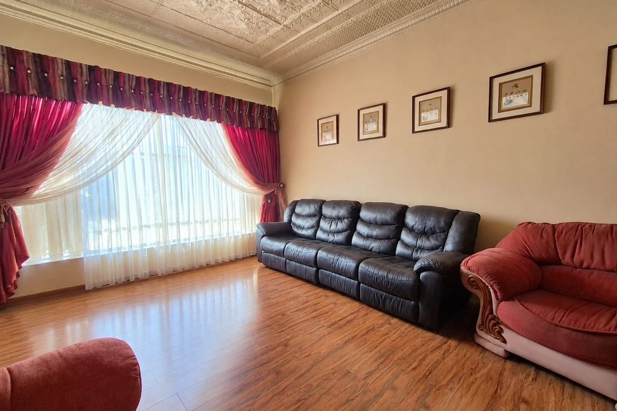 A spacious living room featuring a classic pressed metal ceiling, decorative cornicing, and durable laminate flooring, offering a traditional aesthetic.