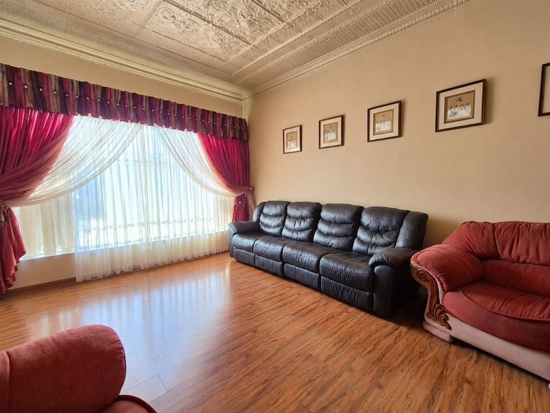 A spacious living room featuring a classic pressed metal ceiling, decorative cornicing, and durable laminate flooring, offering a traditional aesthetic.