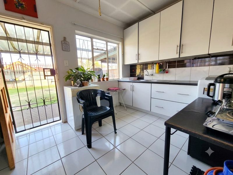 A functional laundry area featuring white built-in cabinetry, tiled flooring, a sink, and direct access to the rear garden through a security gate.