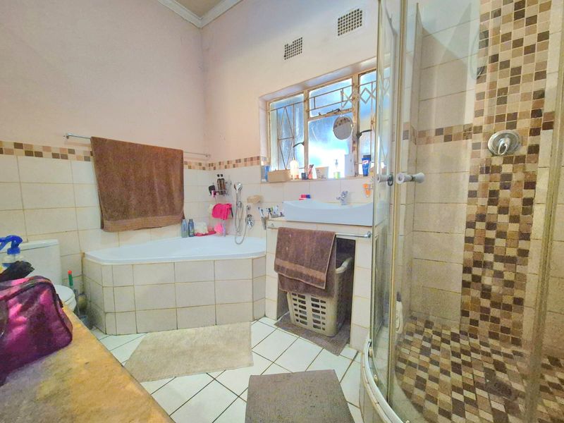 A functional bathroom featuring a corner bathtub, separate shower enclosure, and wall-mounted basin with tiled finishes throughout.