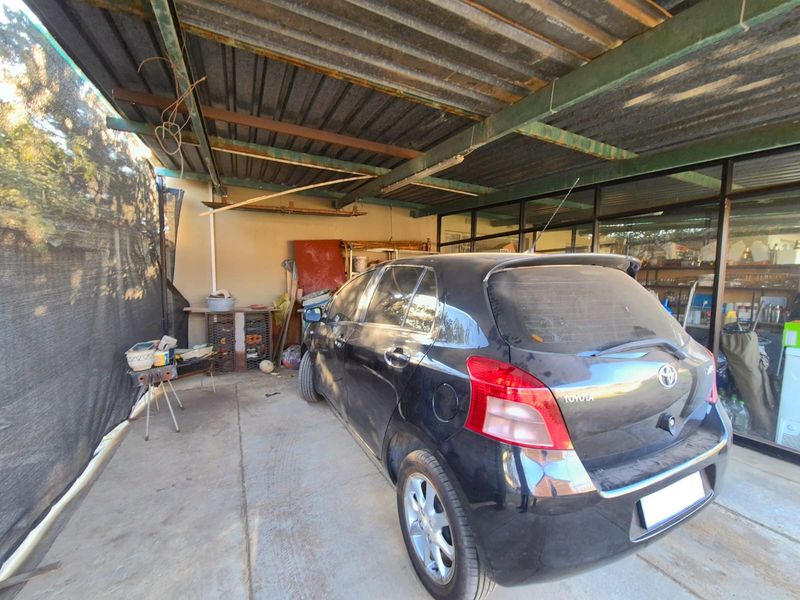 A covered outdoor parking area featuring a corrugated metal roof, steel support structure, and concrete flooring.