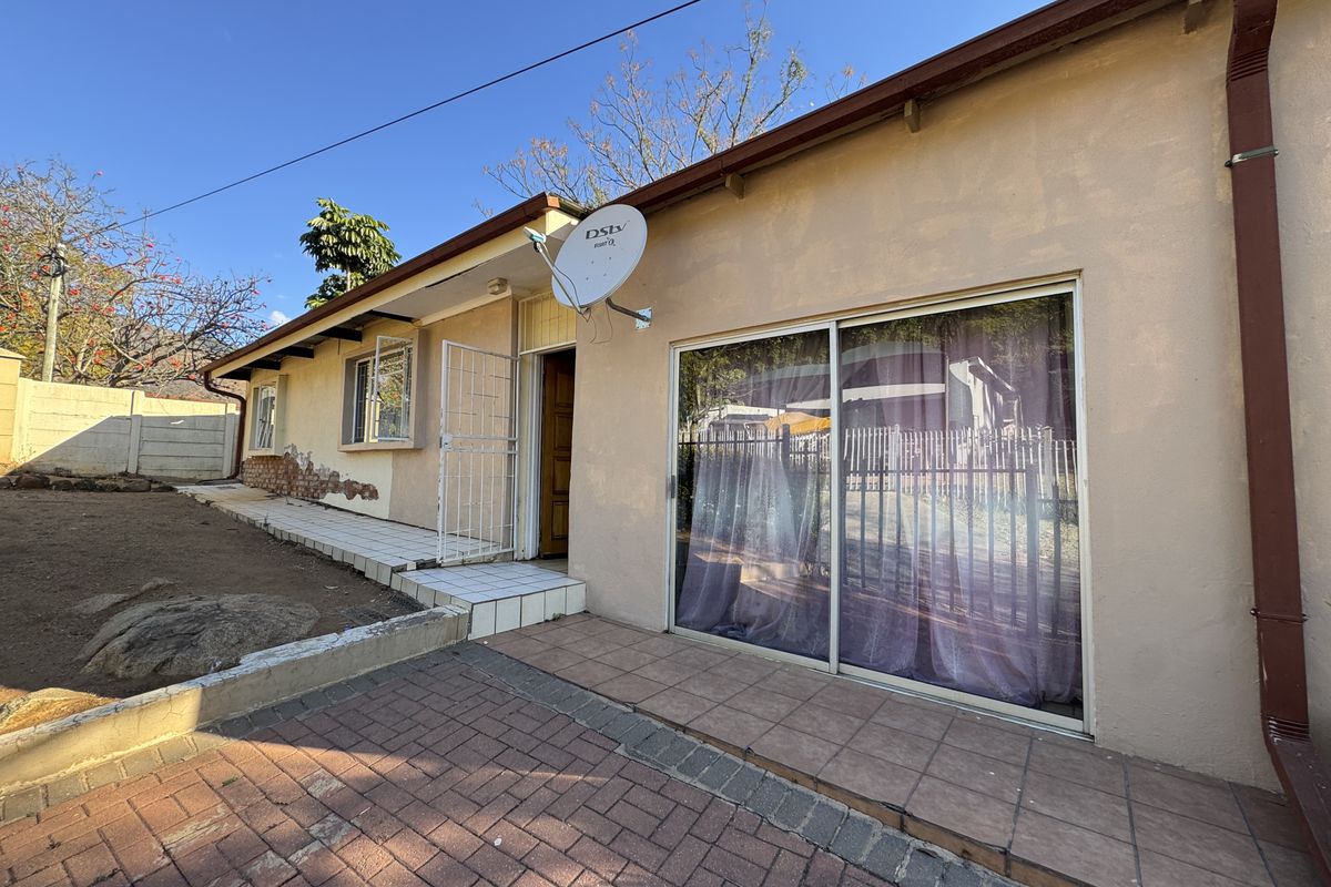 Rear exterior view of the property featuring a paved patio area, sliding glass door access, and visible exterior wall maintenance requirements.