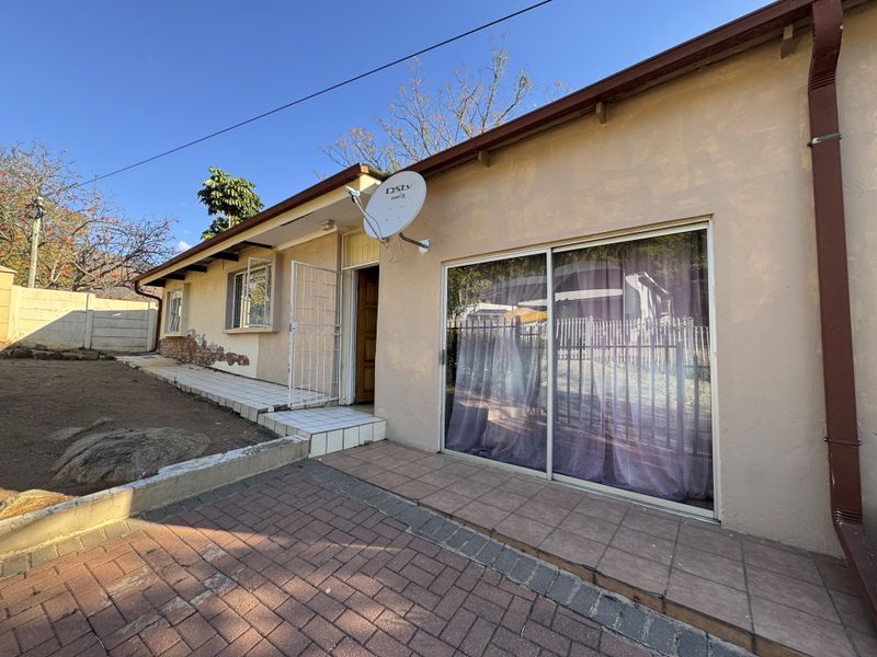 Rear exterior view of the property featuring a paved patio area, sliding glass door access, and visible exterior wall maintenance requirements.