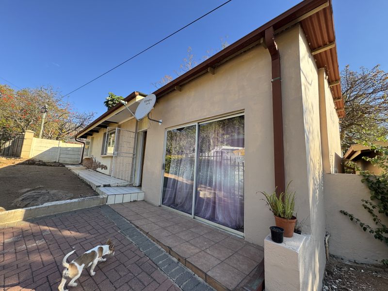 Rear exterior view of the house featuring a tiled patio area, sliding glass doors, and security gate access.