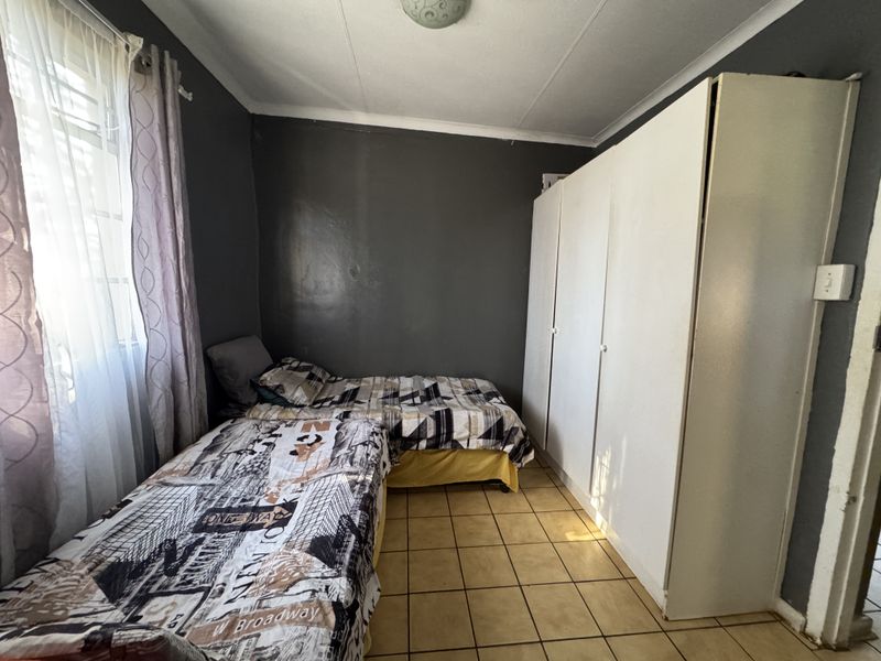 A functional bedroom featuring built-in cupboards, tiled flooring, and dark-toned walls, providing a practical space with potential for cosmetic updates.