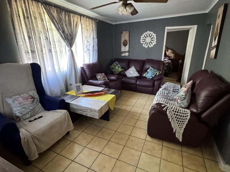 A living room featuring ceramic floor tiles, a ceiling fan, and large windows with curtain rails, offering a functional space for relaxation.