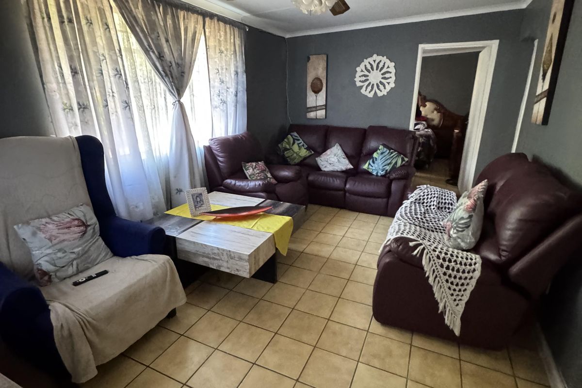 A living room featuring ceramic floor tiles, a ceiling fan, and large windows with curtain rails, offering a functional space for relaxation.