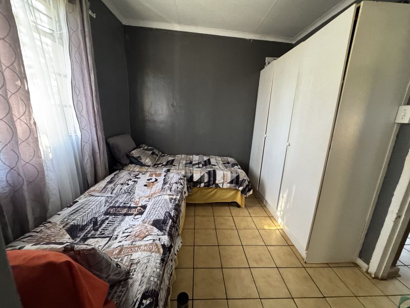 A bedroom featuring tiled flooring, a built-in wardrobe, and dark-toned walls, offering a functional space with potential for cosmetic updates.
