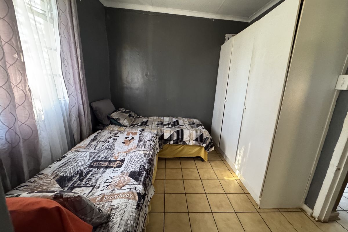 A bedroom featuring tiled flooring, a built-in wardrobe, and dark-toned walls, offering a functional space with potential for cosmetic updates.