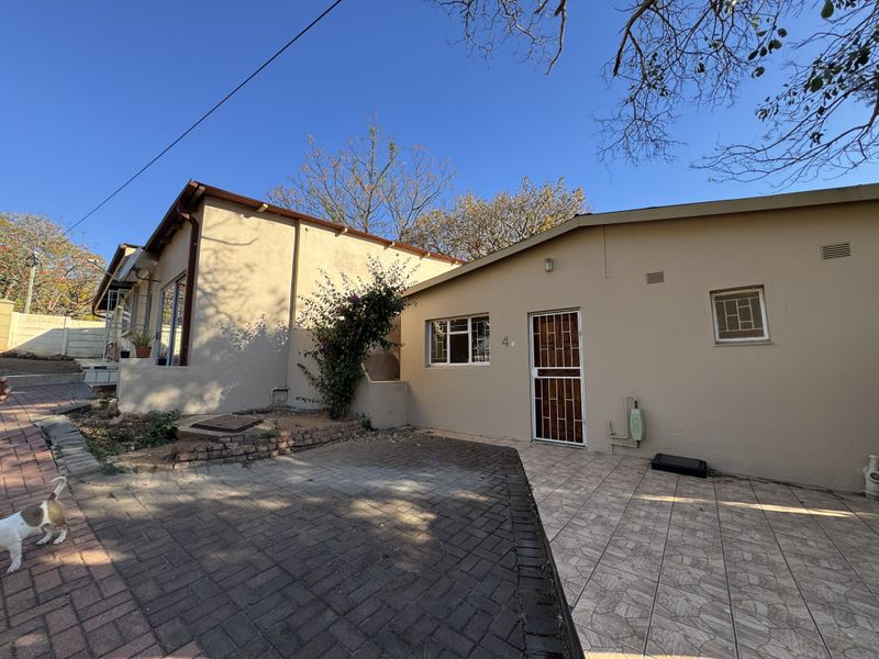 Rear exterior view of the property featuring a paved patio area, security gate, and brick driveway access.