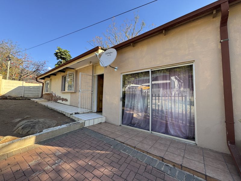 Rear exterior view of the house featuring a tiled patio, sliding glass door, security gate, and brick paved area with visible wall plaster damage.