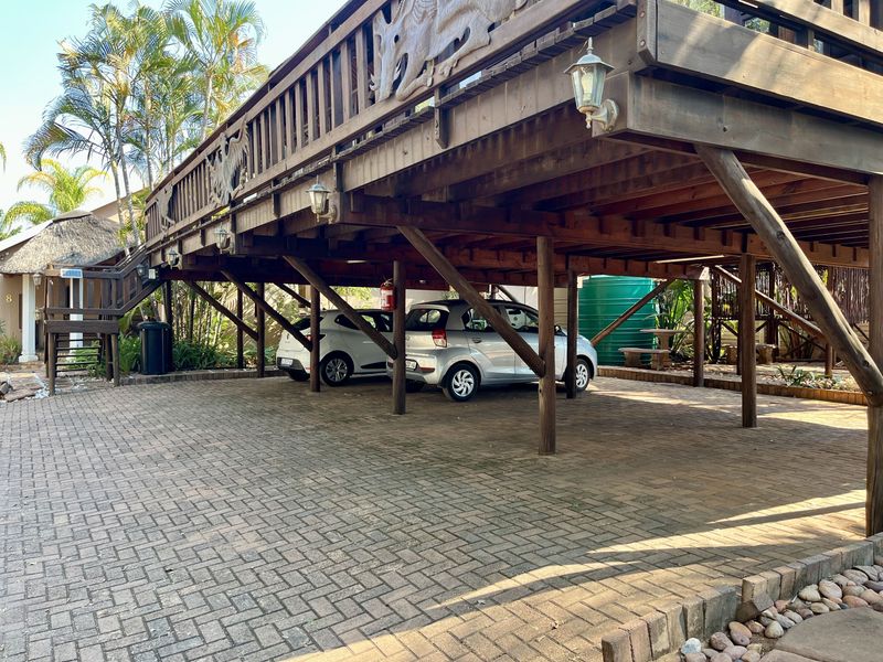Covered parking area situated beneath a raised timber deck, featuring paved flooring and a water storage tank.