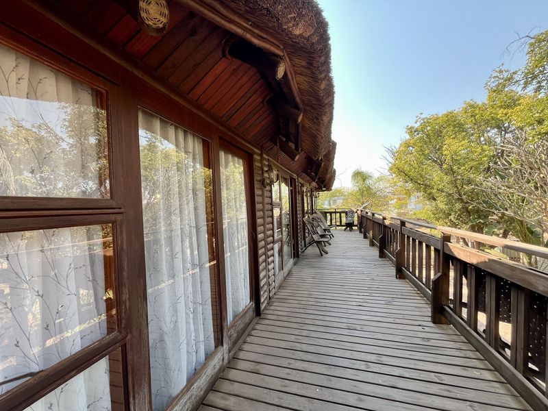 A spacious wooden balcony featuring timber decking, a protective balustrade, and a traditional thatched roof overhang, providing an elevated outdoor living space.