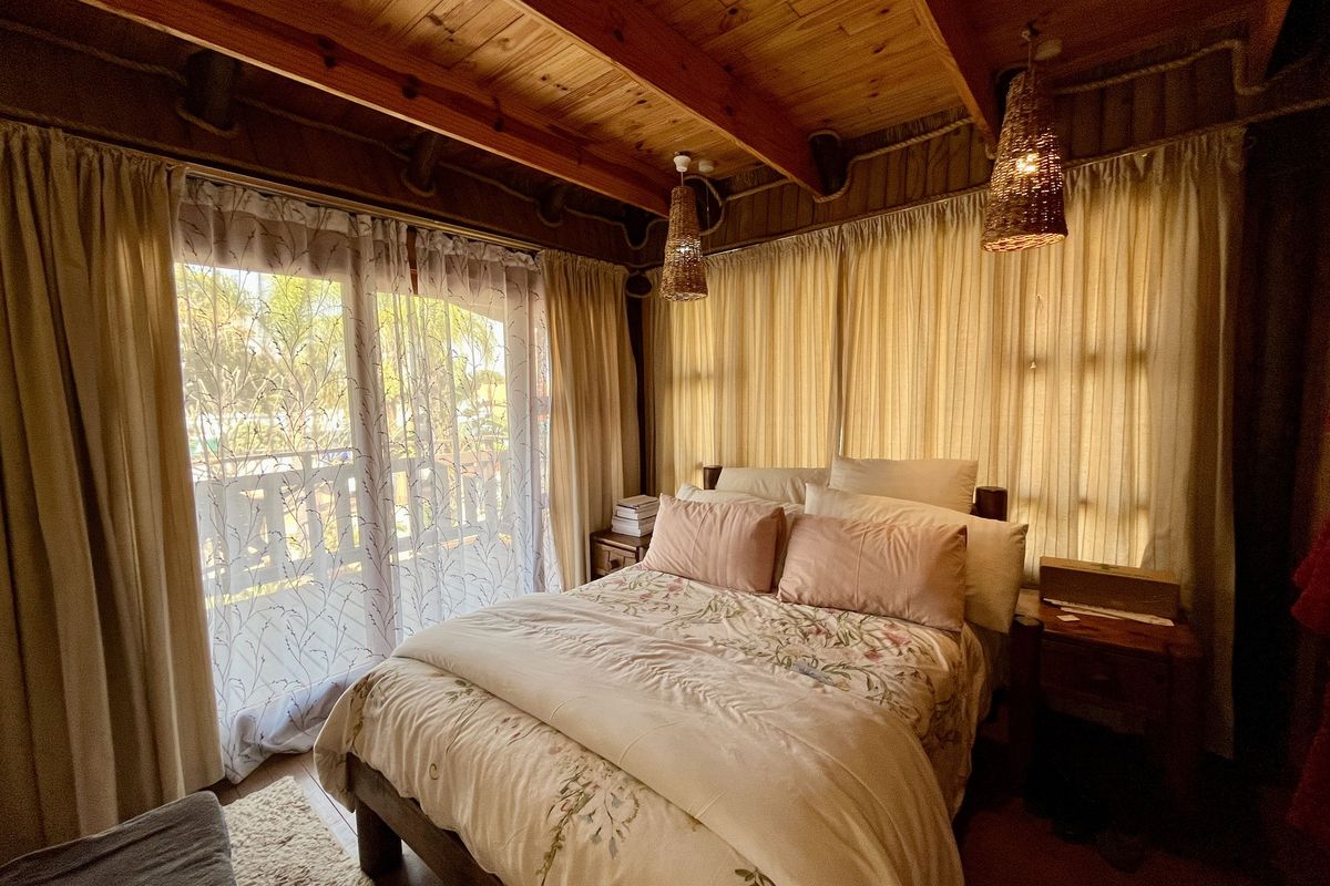 Cozy bedroom featuring exposed timber ceiling beams and a sliding glass door providing natural light and access to an outdoor area.
