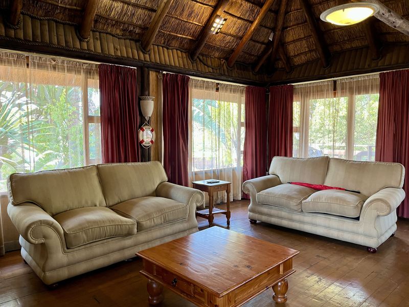A cozy living room featuring a traditional thatched roof with exposed timber beams, hardwood flooring, and large windows providing ample natural light.