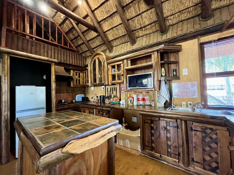 Rustic kitchen featuring a high thatched ceiling with exposed timber beams, custom timber cabinetry, a tiled island, and integrated kitchen appliances.