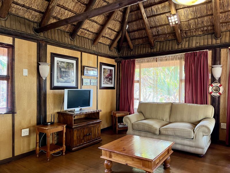 A cozy living room featuring a traditional thatched roof with exposed timber beams, wood-paneled walls, and warm timber flooring.