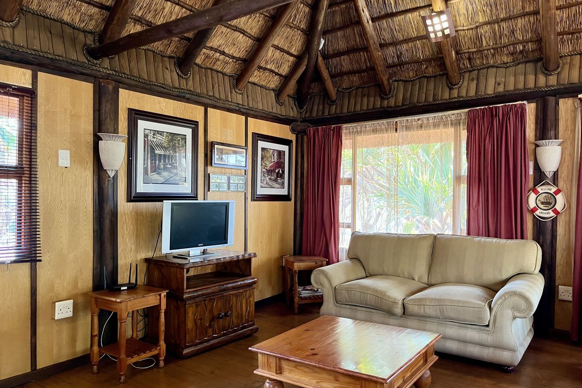 A cozy living room featuring a traditional thatched roof with exposed timber beams, wood-paneled walls, and warm timber flooring.