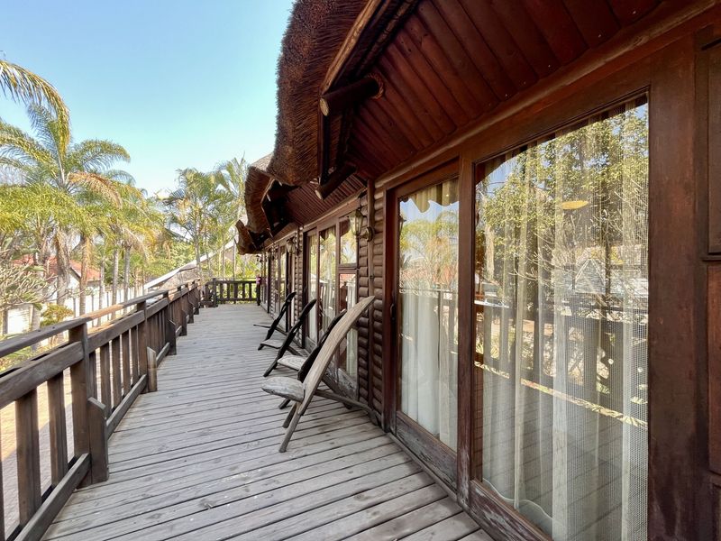 A spacious timber balcony featuring a thatched roof overhang, wooden balustrades, and large sliding glass doors providing access to the interior.
