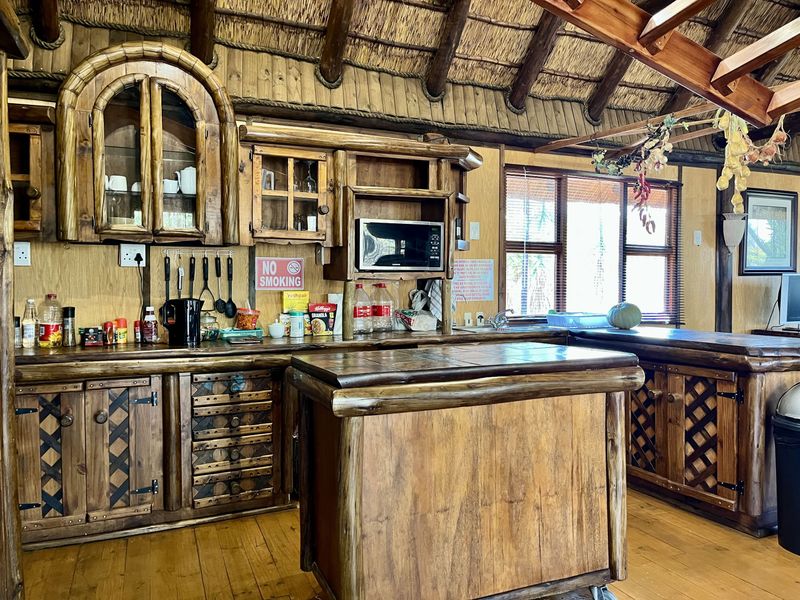 Rustic kitchen featuring custom timber cabinetry, a central timber island, and a traditional thatched roof with exposed wooden beams.