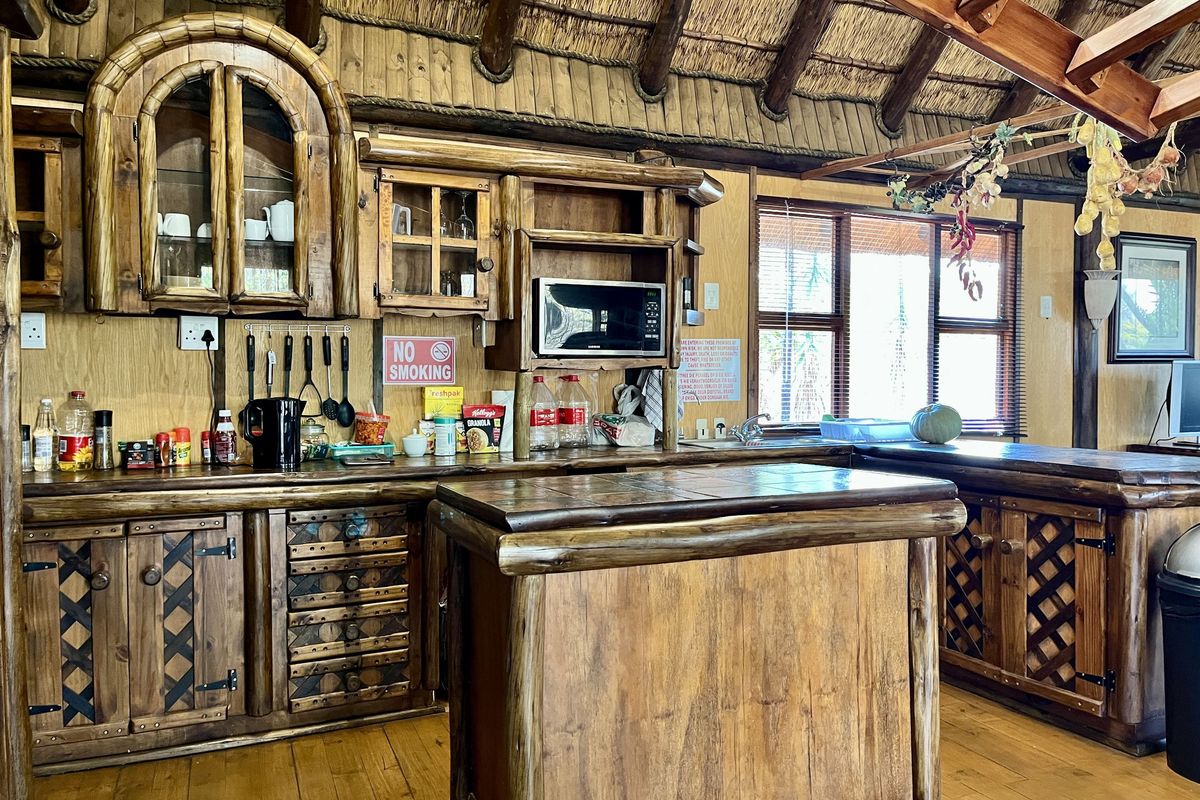 Rustic kitchen featuring custom timber cabinetry, a central timber island, and a traditional thatched roof with exposed wooden beams.