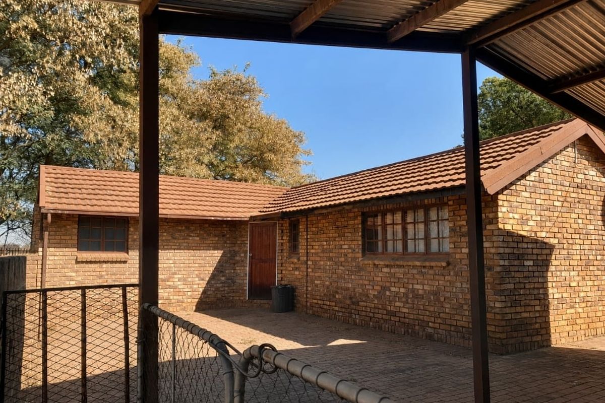 A view of the rear exterior featuring a face brick building with a tiled roof and a covered paved patio area.