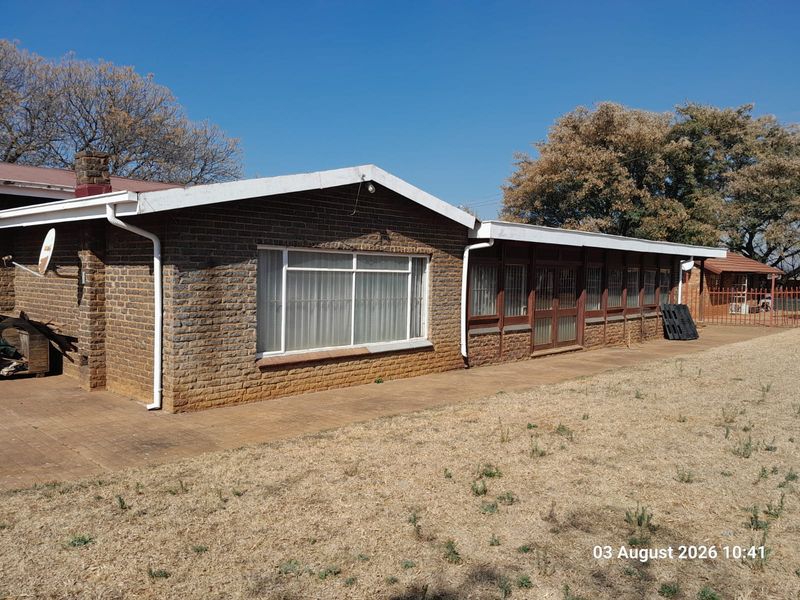 Rear view of a single-story brick farmhouse featuring a paved patio area, guttering, and security bars on the windows.