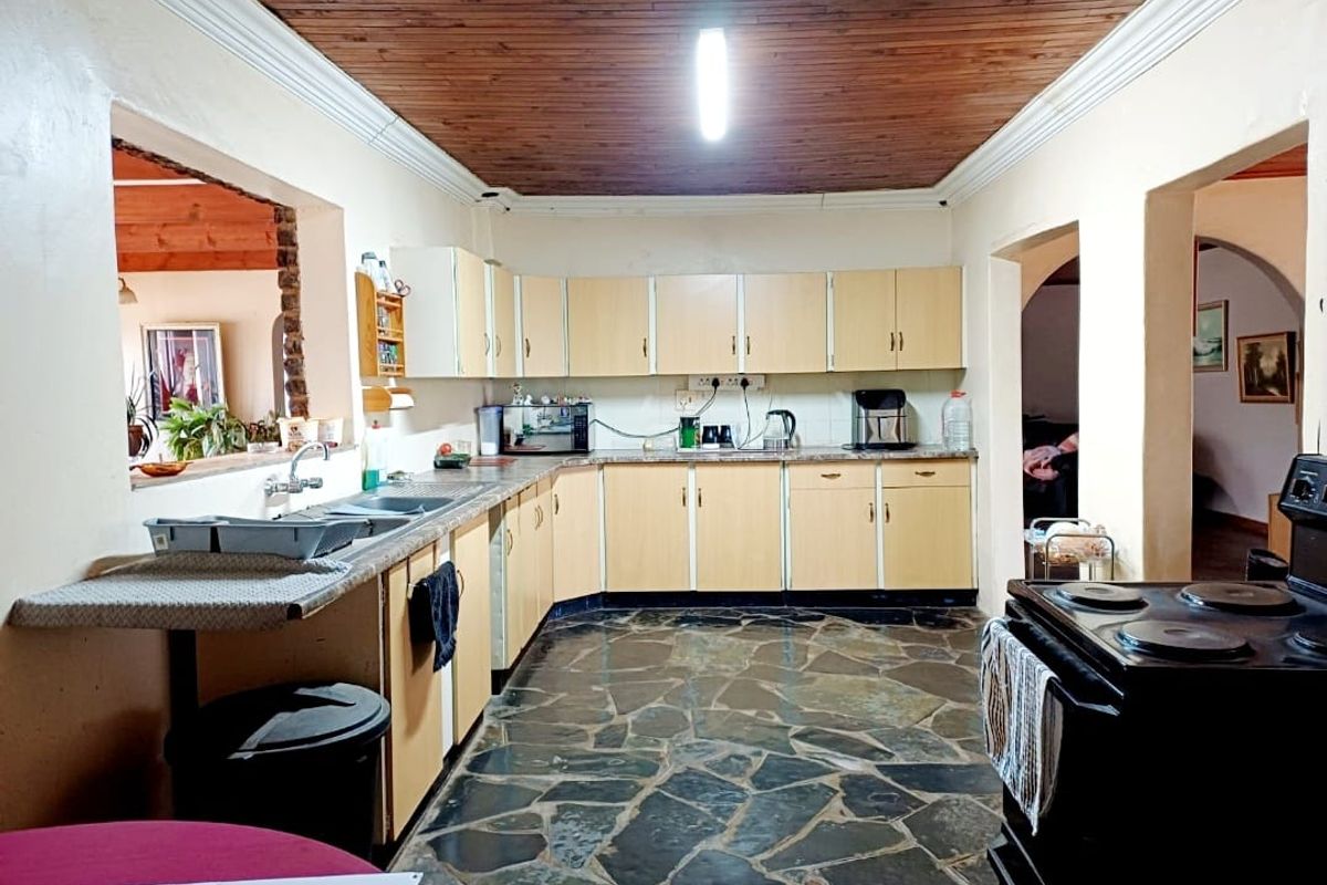 A functional kitchen featuring timber ceiling panels, stone tile flooring, and ample built-in cabinetry with laminate countertops.