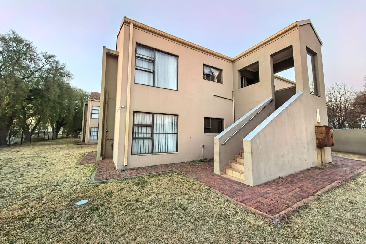 Rear view of a multi-story flat building featuring plastered walls, aluminium windows, and an external staircase with brick paved surrounds.
