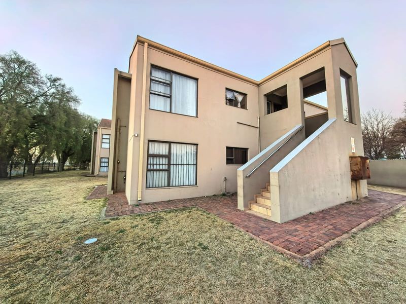 Rear view of a multi-story flat building featuring plastered walls, aluminium windows, and an external staircase with brick paved surrounds.