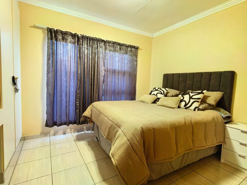 A bedroom featuring tiled flooring, built-in cupboards, and a ceiling light fixture, providing a functional and neutral living space.