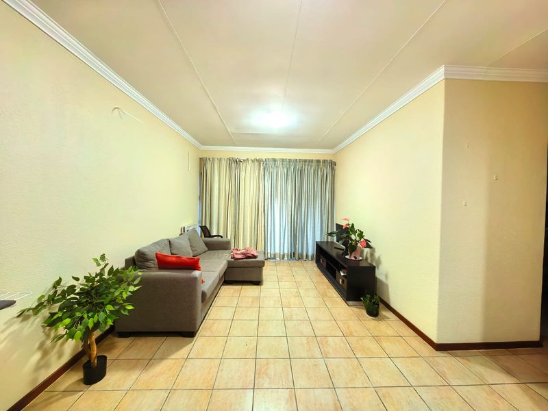 A living room featuring ceramic floor tiles, ceiling cornicing, and large window curtains, providing a neutral base for interior updates.