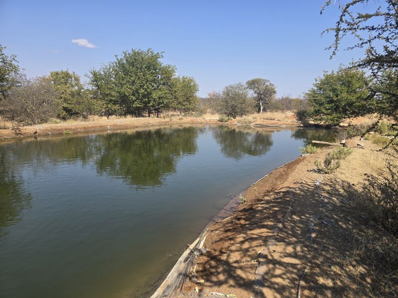 A natural earthen farm dam or reservoir featuring a visible liner and surrounding rural landscape.