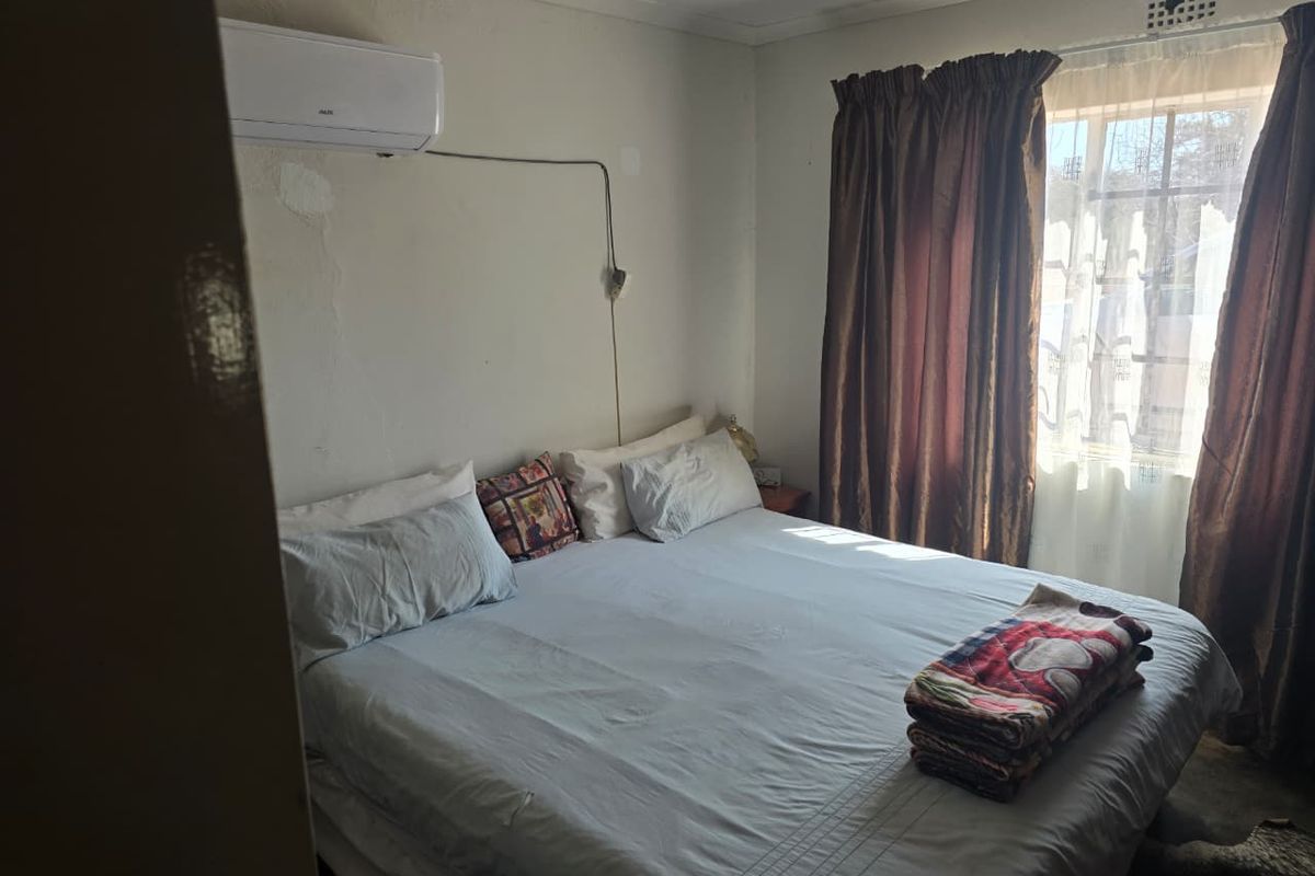 A bedroom featuring a wall-mounted air conditioning unit and window security bars, showing signs of wear on the wall surfaces.