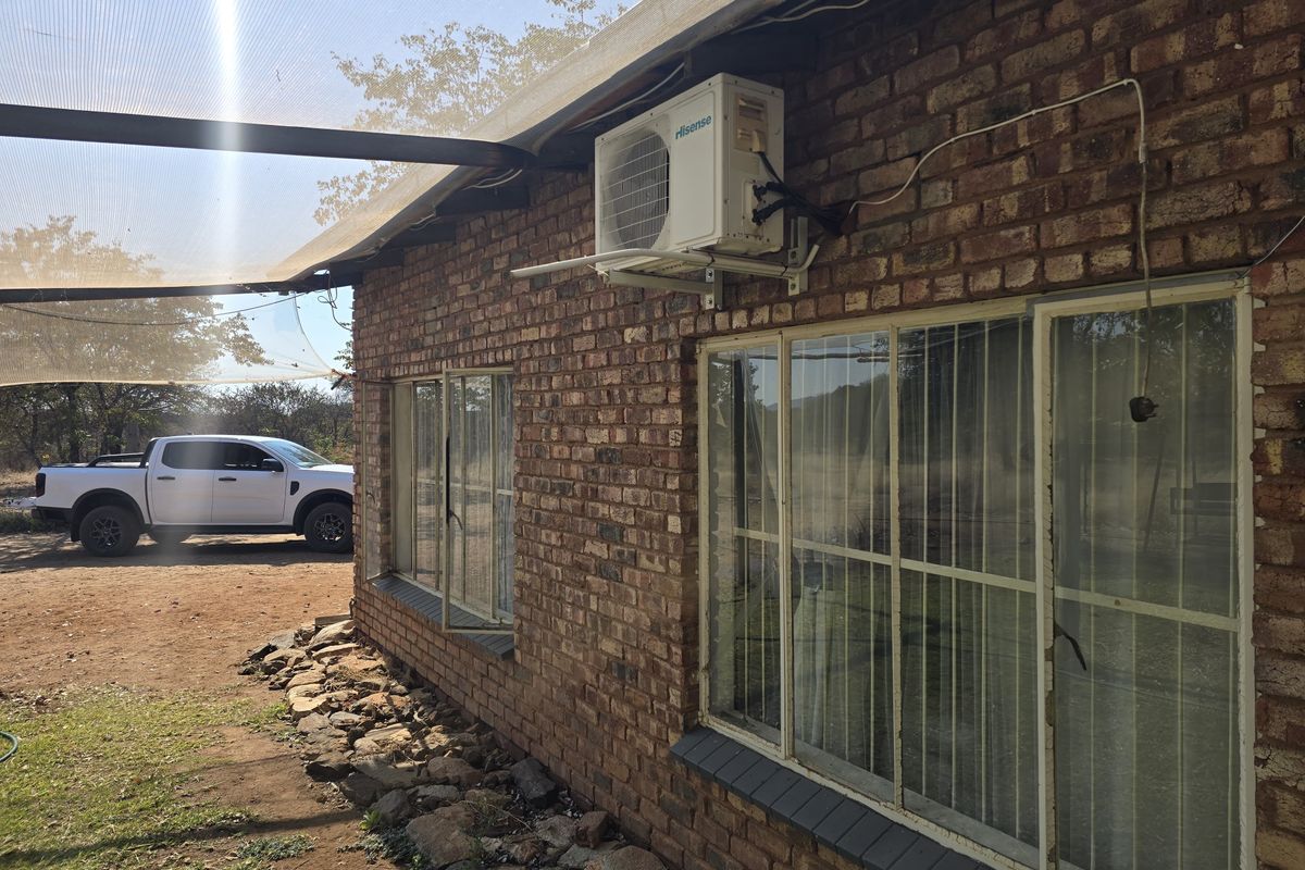 Exterior view of a face brick farm building featuring an installed air conditioning unit, aluminium windows with security bars, and an overhead shade cloth structure.