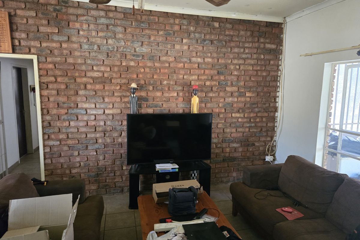 Living room featuring an exposed brick feature wall, tiled flooring, and a ceiling fan, with some visible electrical wiring requiring attention.