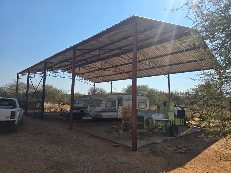 Open-sided steel-framed farm shed with a corrugated metal roof and concrete slab, suitable for vehicle or equipment storage.